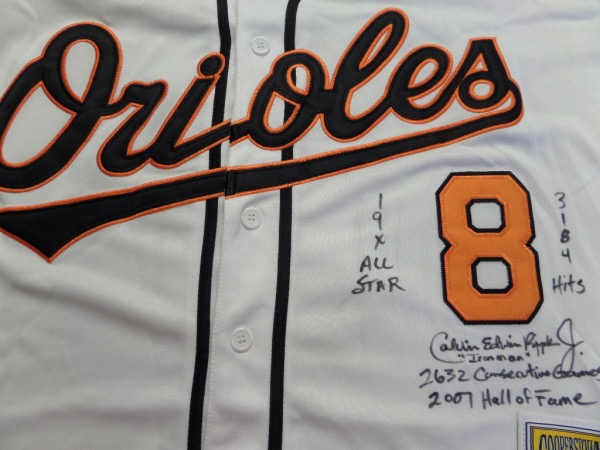 This 2001 size L white throwback O's jersey from Mitchell & Ness is in NM condition, and comes trimmed in black and orange, with everything sewn.  It comes hand-signed on the front in black sharpie by the HOF ss/3b himself, grading a legible, and including 19X All Star, 3184 Hits, "Ironman", 2632 Consecutive Games and 2007 Hall of Fame ... not to mention that he signed a RARE, full name Calvin Edwin Ripken Jr. signature.  AWESOME and unique, and super cool!