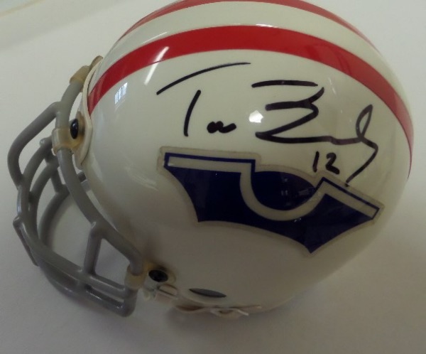 This mostly white Sarco style mini football helmet features a double red stripe down the middle, and a throwback original 1960 Pats logo in blue affixed to either side.  It comes hand-signed in black sharpie by the man who brought SIX Super Bowl titles to the Atlantic Northeast, Tom Brady, and the signature grades about a 7.5 overall.  Valued into the mid/high hundreds!
